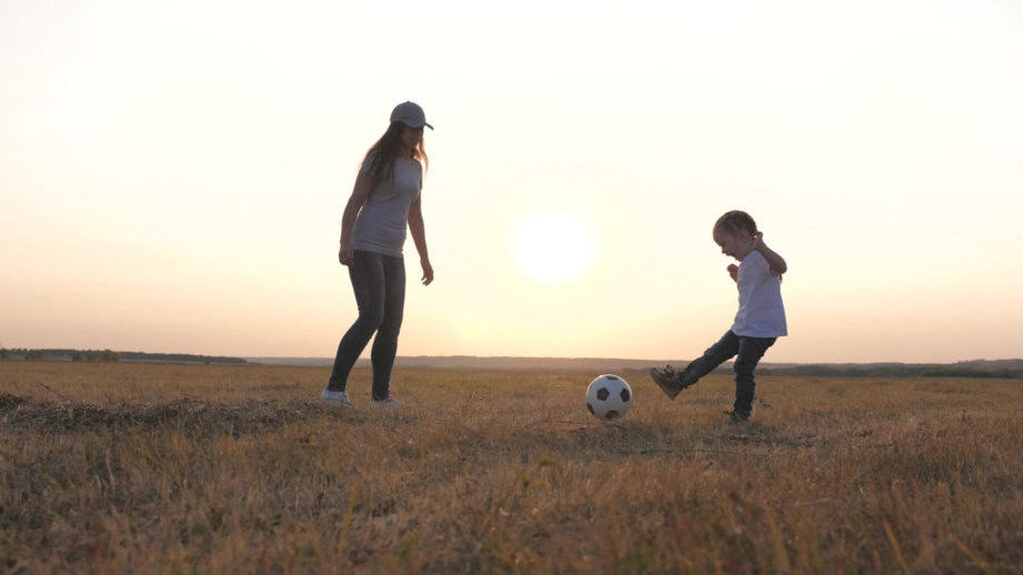 mom playing soccer with daughter at sunset