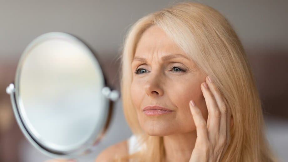 older woman looking at skin in mirror